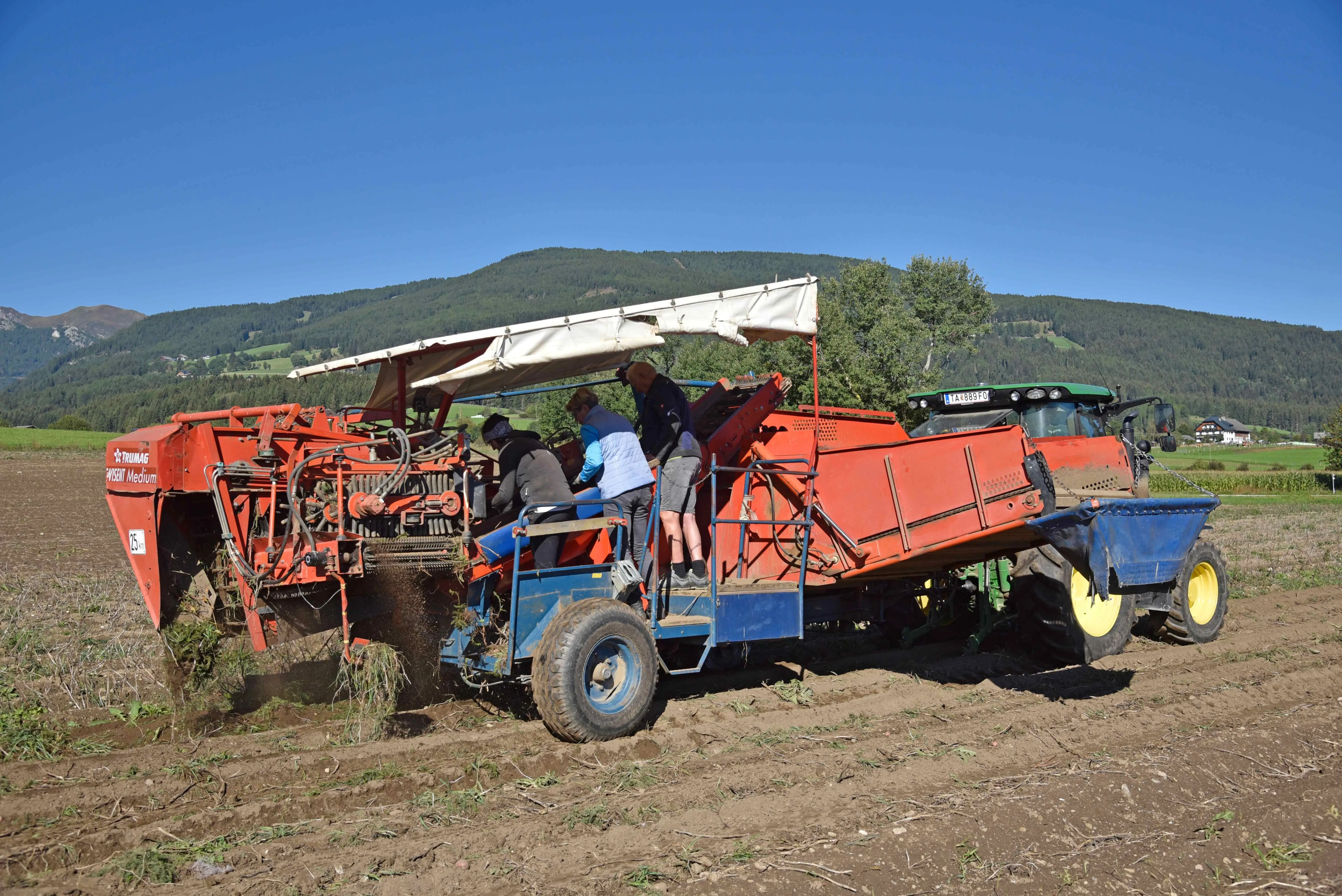 Lungauer Eachtling Arbeit am Feld, rollende Erntemaschine mit Menschen