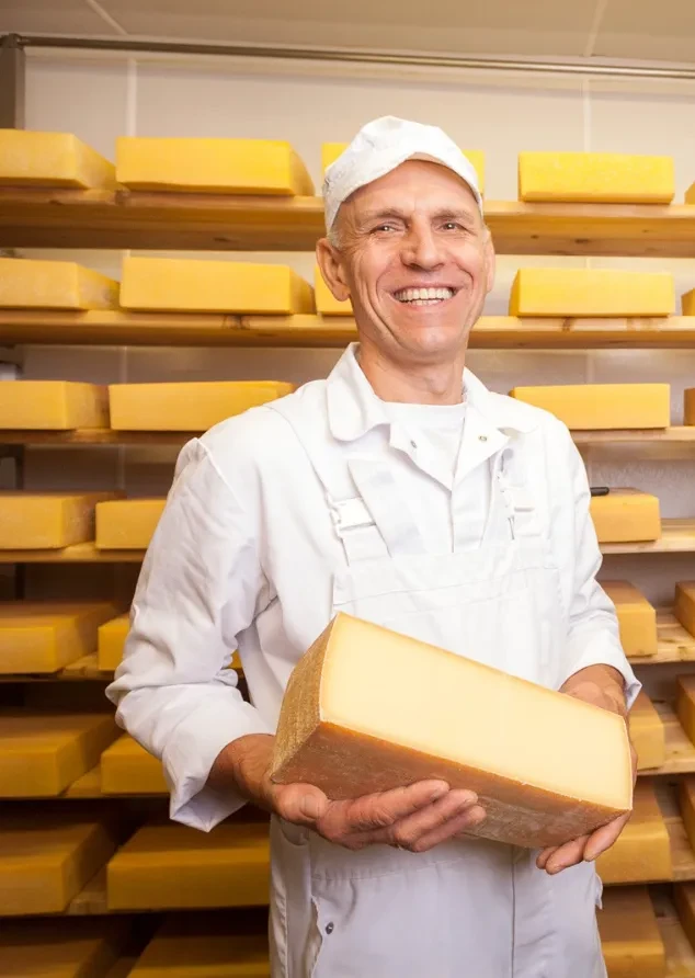 Dorfkäserei Pötzelsberger lachender Franz mit Käse im Reiferaum