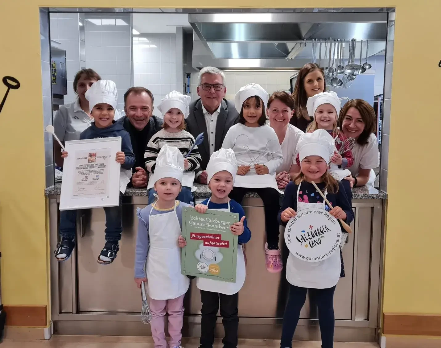 Für dieses gelebte Bewusstsein rundum eine bestmögliche Ernährung aus der Region wurde am 16.11.2023 vom Salzburger Agrar Marketing die SalzburgerLand Herkunftstafel „Ausgezeichnet aufgetischt“ verliehen. Bild Tafelverleihung: Im Kreis der Kinder und des Küchenpersonals des Kindergarten Liefering 2, Salzburgs Vizebürgermeister Bernhard Auinger, Landesrat Josef Schwaiger und Kindergarten-Leiterin Kerstin Hager (hinten rechts).