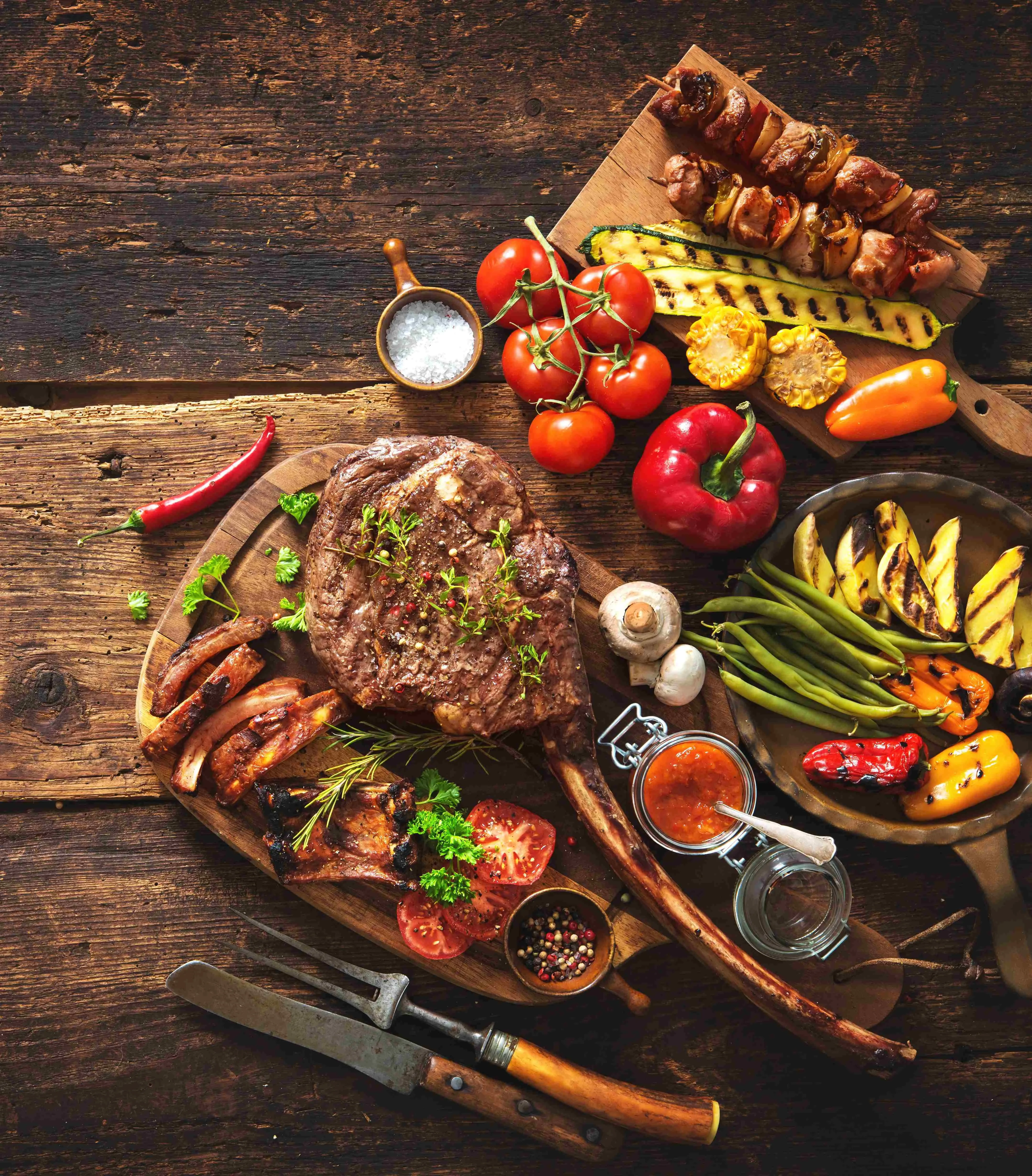 Grill Sujet mit gegrillte Fleisch, Gemüse, Spieße, Saucen, Salz, Besteck, Holzbrett am Holztisch